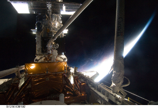 Hubble Repair: A NASA astronaut installing Hubble's corrective optics.  The Sun is rising over the Earth in the background.